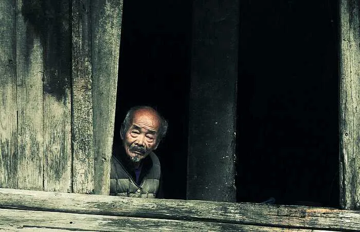 An elder looking through an old wooden window.